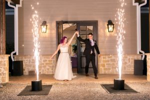 A bride and groom standing in front of a house with sparklers, surrounded by DC DJs.